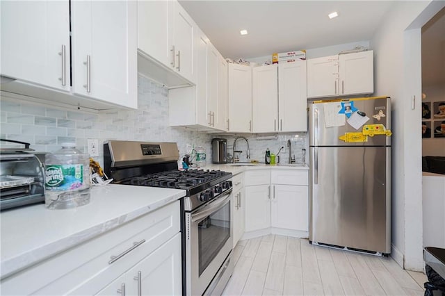 kitchen with a sink, white cabinetry, light countertops, appliances with stainless steel finishes, and decorative backsplash