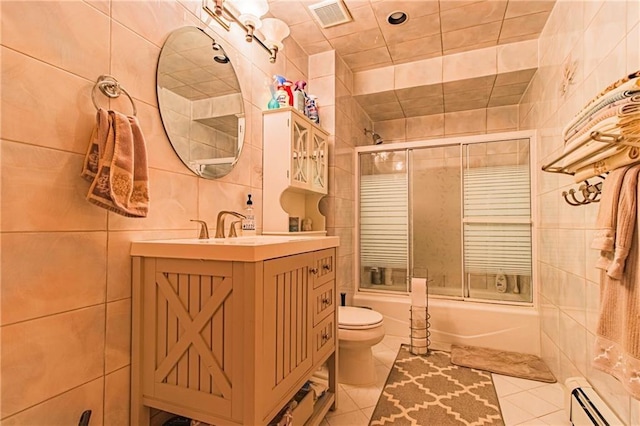 full bathroom with bath / shower combo with glass door, vanity, a baseboard radiator, tile walls, and toilet