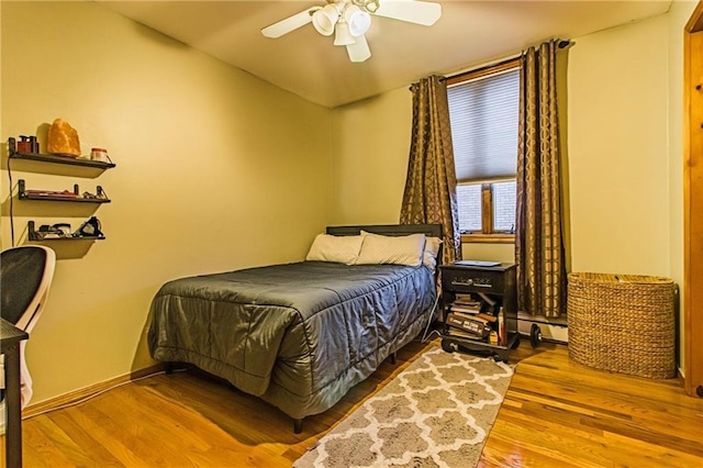 bedroom with light hardwood / wood-style flooring, ceiling fan, and a baseboard heating unit