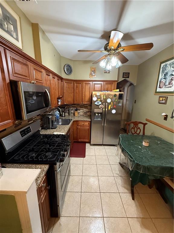 kitchen with appliances with stainless steel finishes, sink, backsplash, light tile patterned floors, and ceiling fan