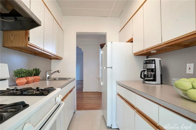 kitchen featuring white appliances, white cabinets, light countertops, under cabinet range hood, and a sink