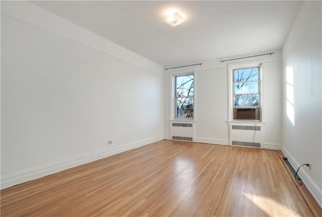 spare room with radiator, light wood-style flooring, baseboards, and cooling unit