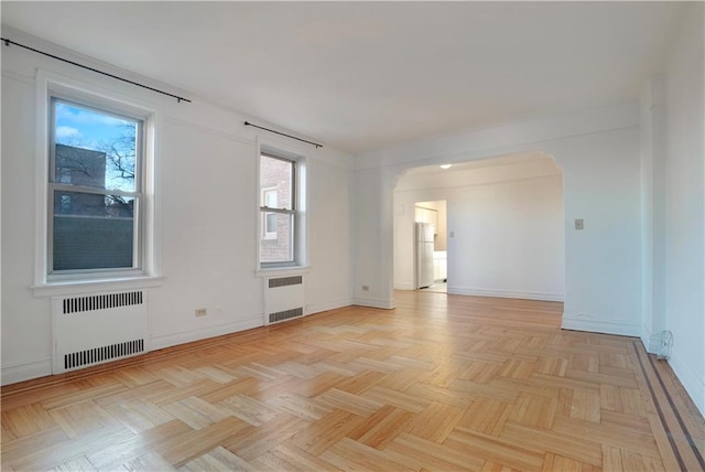 empty room featuring arched walkways, radiator heating unit, and baseboards