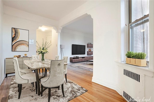 dining space featuring ornate columns, plenty of natural light, light wood-style flooring, and radiator