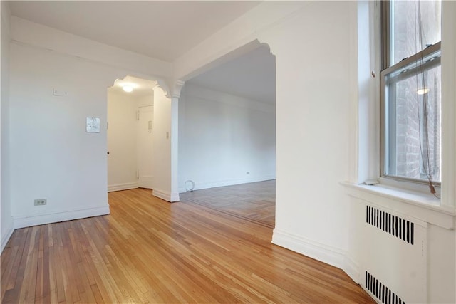 unfurnished room featuring baseboards, decorative columns, light wood-style flooring, and radiator heating unit