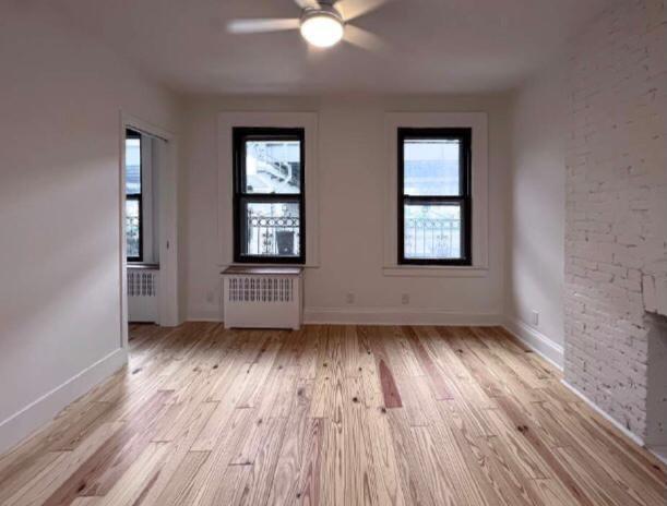 unfurnished room with ceiling fan, radiator heating unit, and light wood-type flooring