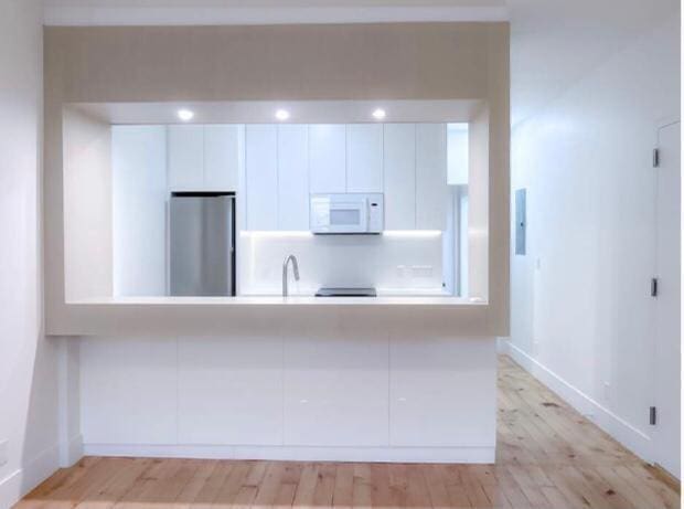 kitchen featuring white cabinets, stainless steel fridge, light wood-type flooring, and sink