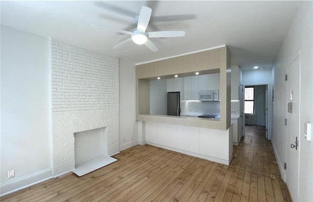 unfurnished living room with a brick fireplace, ceiling fan, and light wood-type flooring