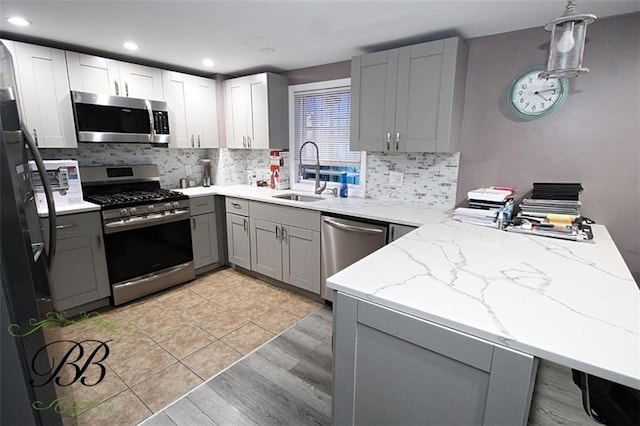 kitchen featuring gray cabinetry, sink, light stone countertops, appliances with stainless steel finishes, and kitchen peninsula