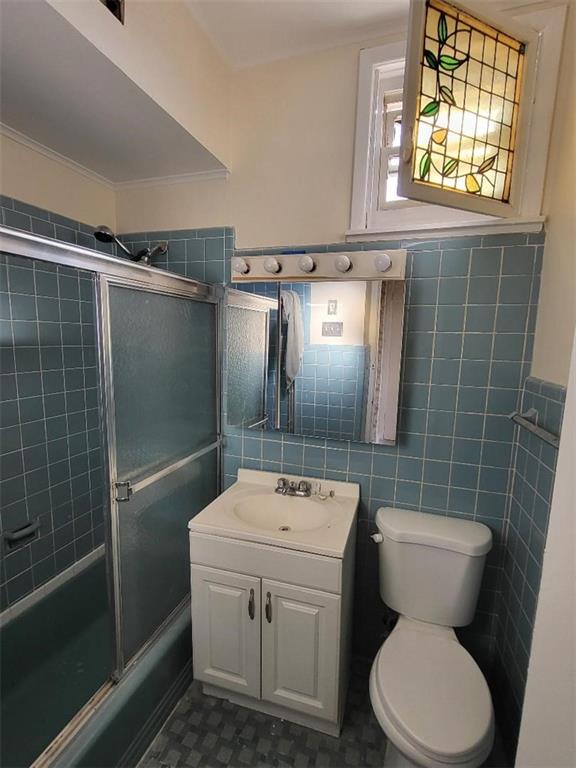 full bathroom featuring toilet, vanity, bath / shower combo with glass door, and tile walls