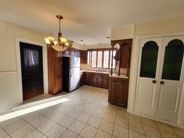 kitchen featuring sink, decorative light fixtures, light tile patterned floors, stainless steel fridge, and a notable chandelier