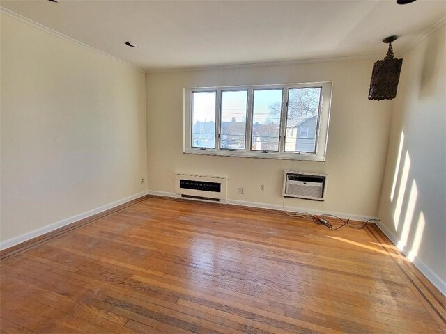 unfurnished room with heating unit, a wall mounted air conditioner, ornamental molding, and hardwood / wood-style floors