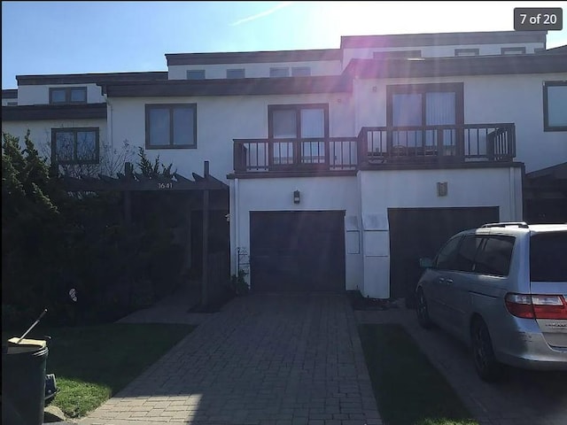 view of front facade with a garage, decorative driveway, a balcony, and stucco siding