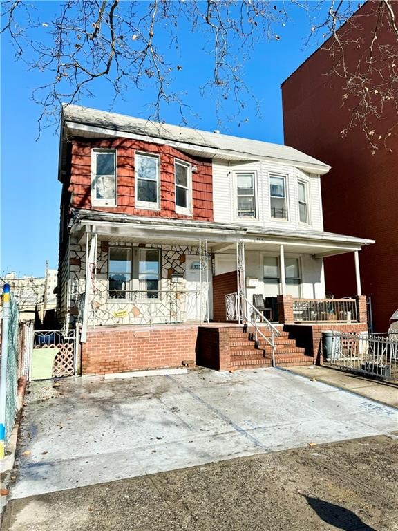 view of front of property featuring covered porch, brick siding, and fence