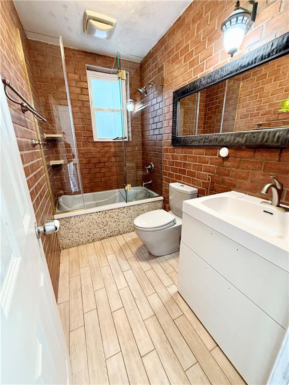 full bathroom with vanity, brick wall, tiled shower / bath combo, and toilet