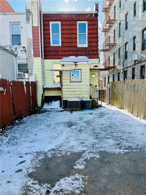 snow covered house with central air condition unit and fence