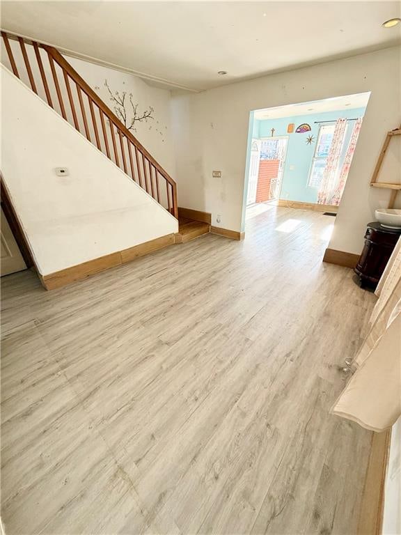 unfurnished living room featuring stairs, light wood-style flooring, and baseboards