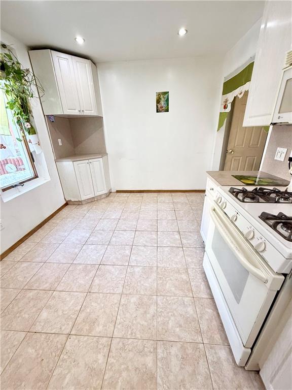 kitchen with white gas stove, recessed lighting, light tile patterned floors, and white cabinetry