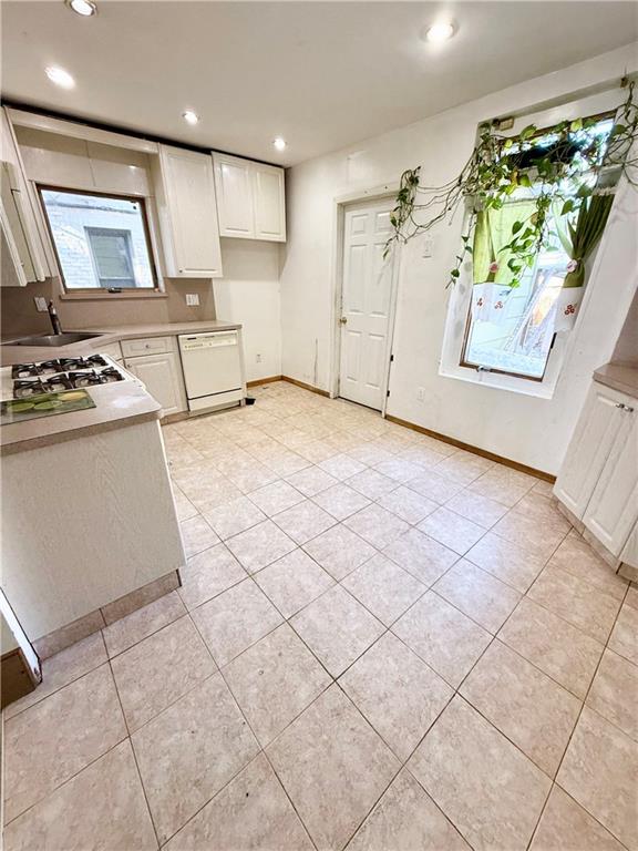 kitchen with white dishwasher, stainless steel gas cooktop, sink, white cabinets, and light tile patterned flooring