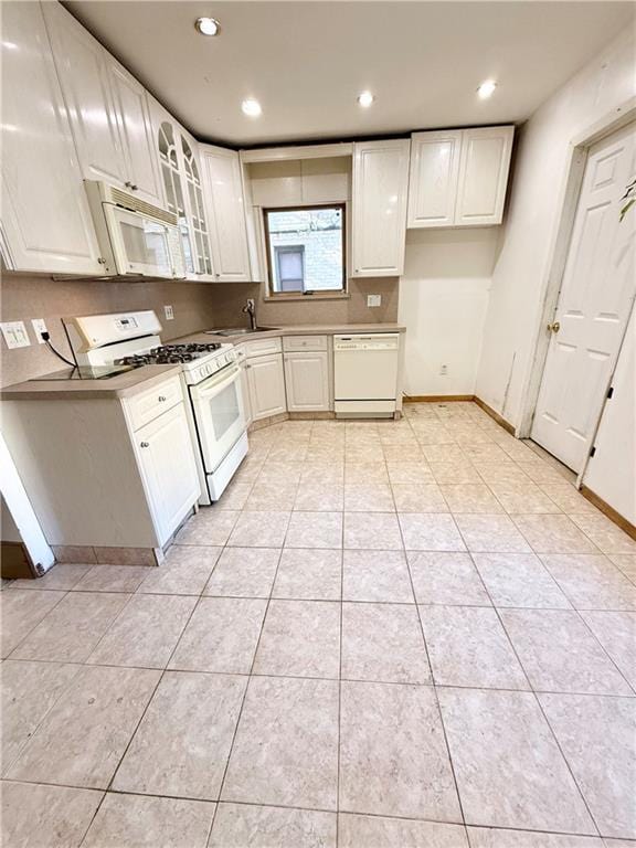 kitchen featuring white appliances, a sink, glass insert cabinets, light tile patterned floors, and baseboards