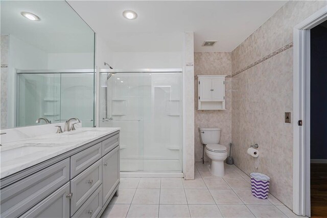 bathroom with tile patterned flooring, toilet, vanity, a shower with shower door, and tile walls