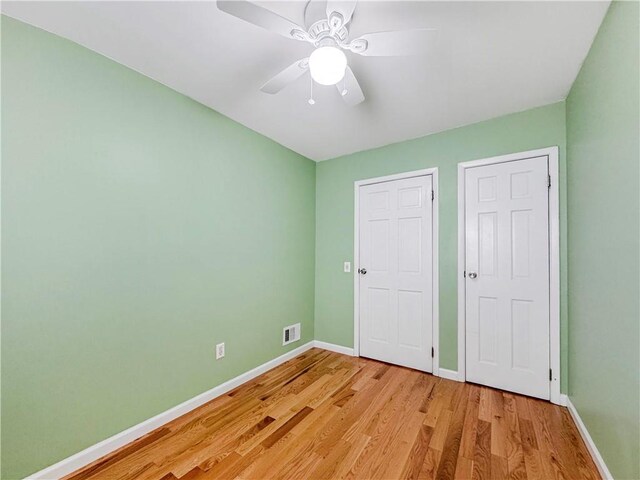 unfurnished bedroom featuring multiple closets, ceiling fan, and light hardwood / wood-style floors