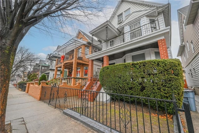 view of front facade featuring brick siding, fence, and a balcony