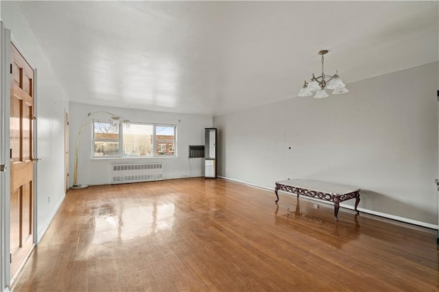 unfurnished living room with an inviting chandelier, radiator heating unit, baseboards, and wood finished floors