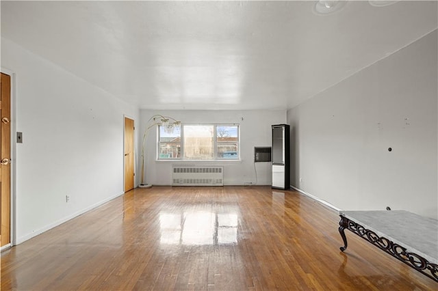 unfurnished living room featuring radiator heating unit, wood finished floors, and baseboards