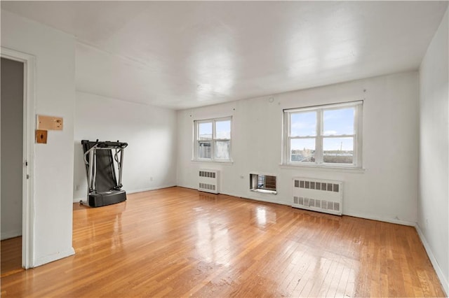 unfurnished living room featuring baseboards, heating unit, wood finished floors, and radiator