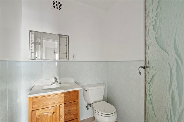 bathroom with toilet, vanity, tile walls, and walk in shower