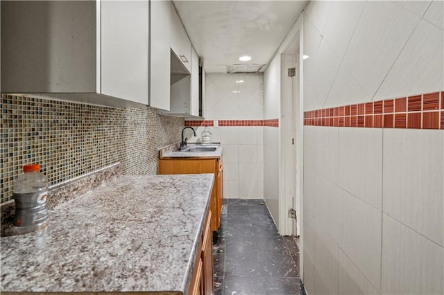 kitchen featuring light countertops, brown cabinetry, a sink, and tile walls