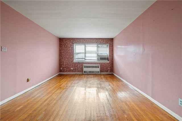 spare room featuring light wood-style floors, radiator, and baseboards