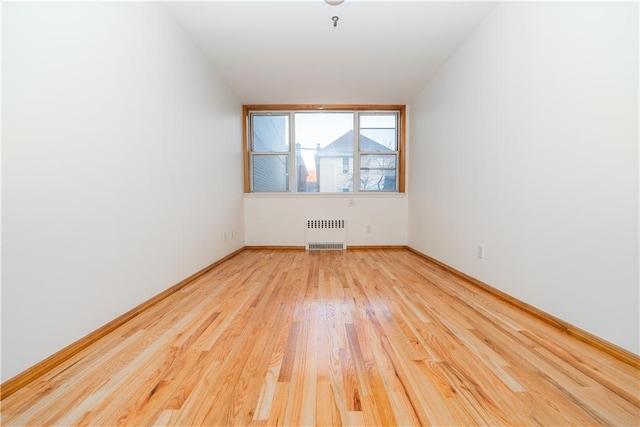 empty room with light wood-style flooring, radiator heating unit, and baseboards