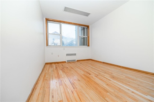 spare room featuring light wood-style flooring, radiator heating unit, visible vents, and baseboards