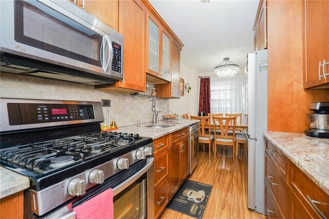 kitchen featuring sink, stainless steel appliances, light stone counters, tasteful backsplash, and light hardwood / wood-style floors