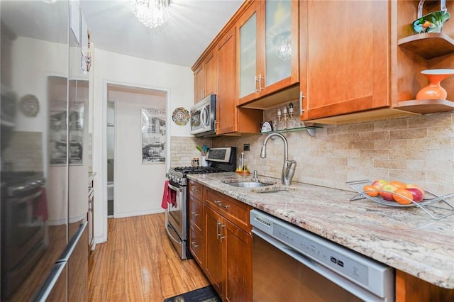 kitchen featuring sink, backsplash, stainless steel appliances, light hardwood / wood-style floors, and light stone countertops