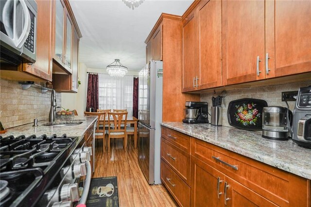 kitchen featuring sink, an inviting chandelier, appliances with stainless steel finishes, light stone countertops, and light hardwood / wood-style floors