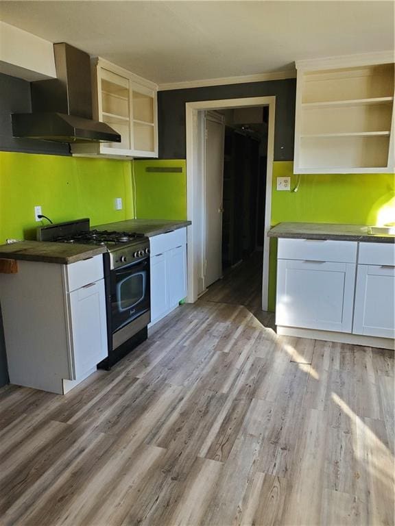 kitchen with white cabinets, gas stove, crown molding, and wall chimney range hood