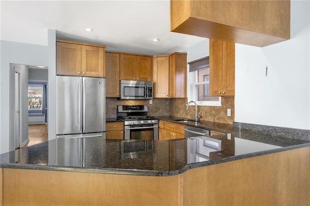 kitchen featuring stainless steel appliances, a sink, a peninsula, and dark stone countertops