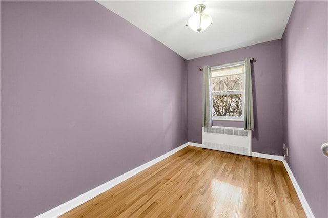 spare room with baseboards, light wood finished floors, and radiator