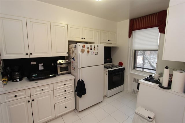 kitchen with radiator, under cabinet range hood, gas range oven, freestanding refrigerator, and white cabinets