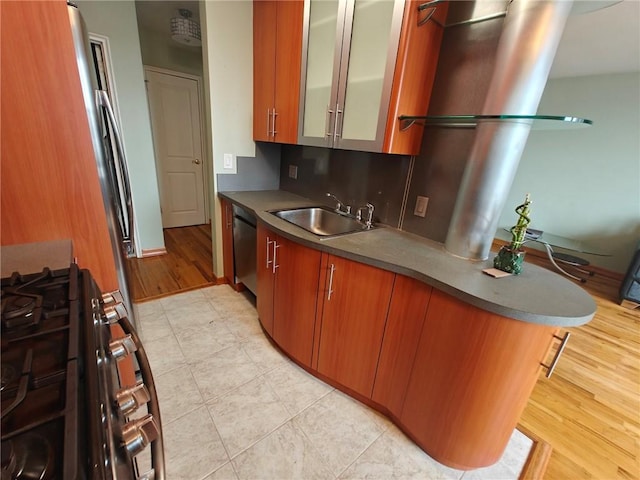 kitchen featuring appliances with stainless steel finishes, brown cabinetry, a sink, and glass insert cabinets