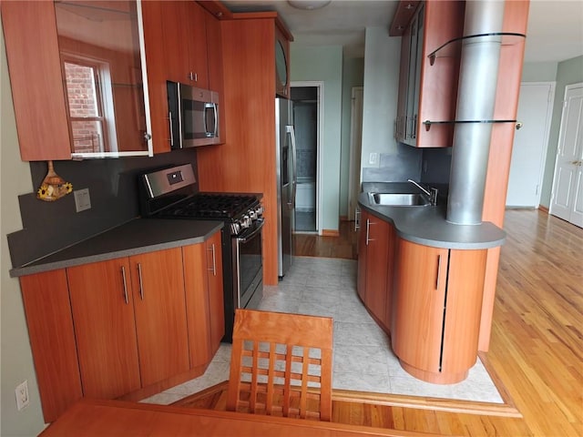 kitchen featuring stainless steel appliances, light wood finished floors, a sink, and brown cabinets