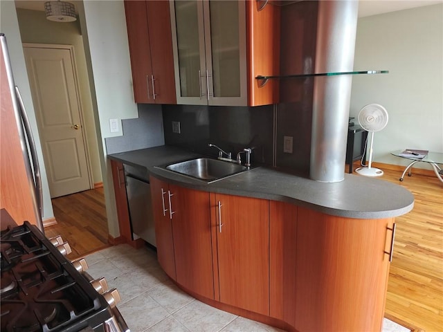 kitchen featuring light wood finished floors, dark countertops, appliances with stainless steel finishes, glass insert cabinets, and a sink