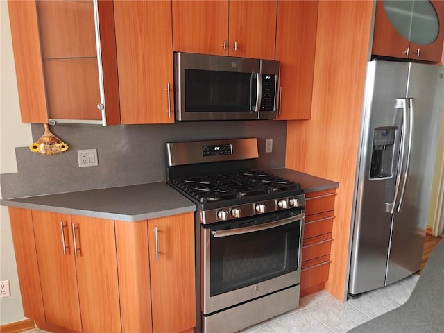 kitchen featuring dark countertops, stainless steel appliances, light tile patterned flooring, and brown cabinets