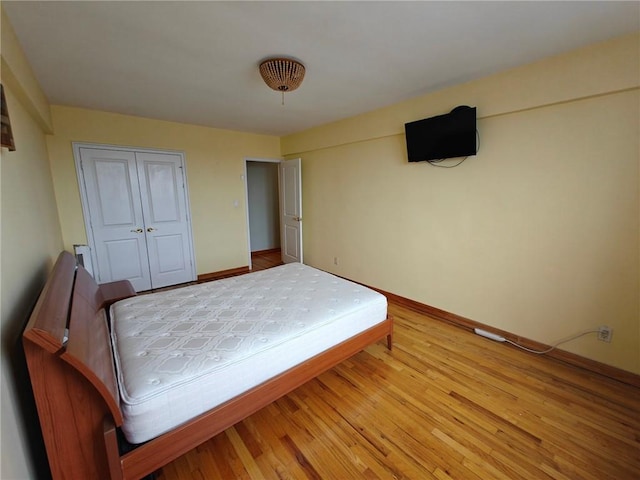 bedroom with light wood-style flooring, baseboards, and a closet