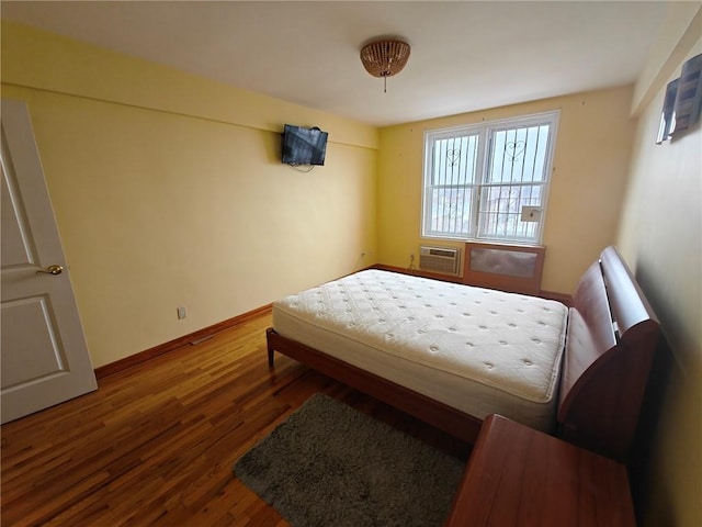 bedroom with an AC wall unit, baseboards, and wood finished floors