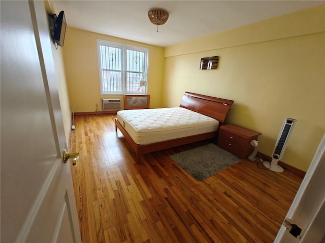 bedroom with an AC wall unit, wood finished floors, and baseboards