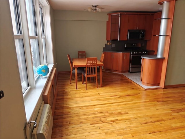 kitchen featuring light wood-style floors, a wall mounted AC, stainless steel microwave, dark countertops, and range with gas cooktop